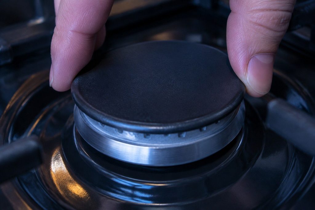 Two fingers lowering a round burner cap squarely onto its base ring on a cooktop and turning it the last few degrees until it sits flat.