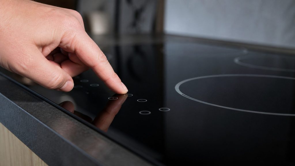 the touch control strip of an electric cooktop close and low, a finger about to rest on it — the 30-inch electric with touch controls