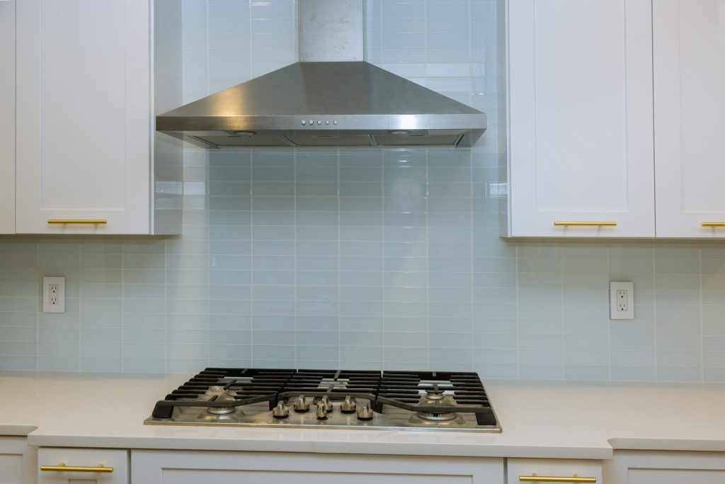 a stainless chimney hood mounted on a wall above a cooktop — the grey SKU