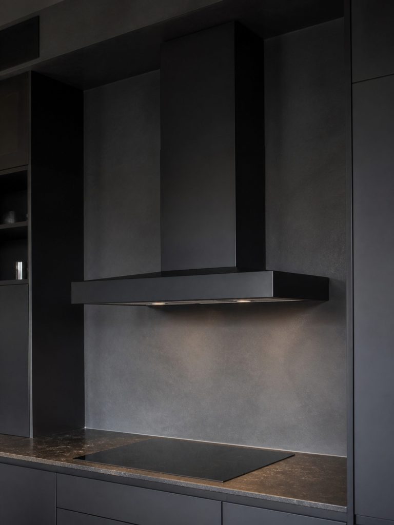a dark-finish wall canopy hood reading as one shape in a near-black kitchen — the deep charcoal SKU