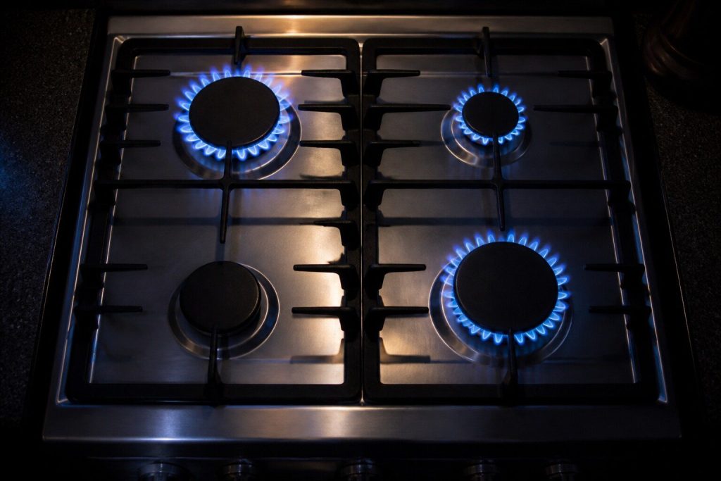 A gas cooktop photographed from above at night with three burner crowns carrying steady blue flame and the fourth completely dark and cold.